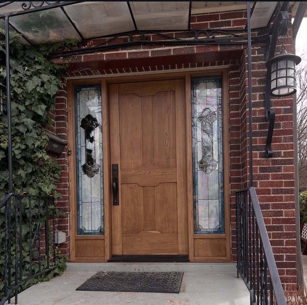 Custom wood entry door with decorative glass sidelights in a brick home