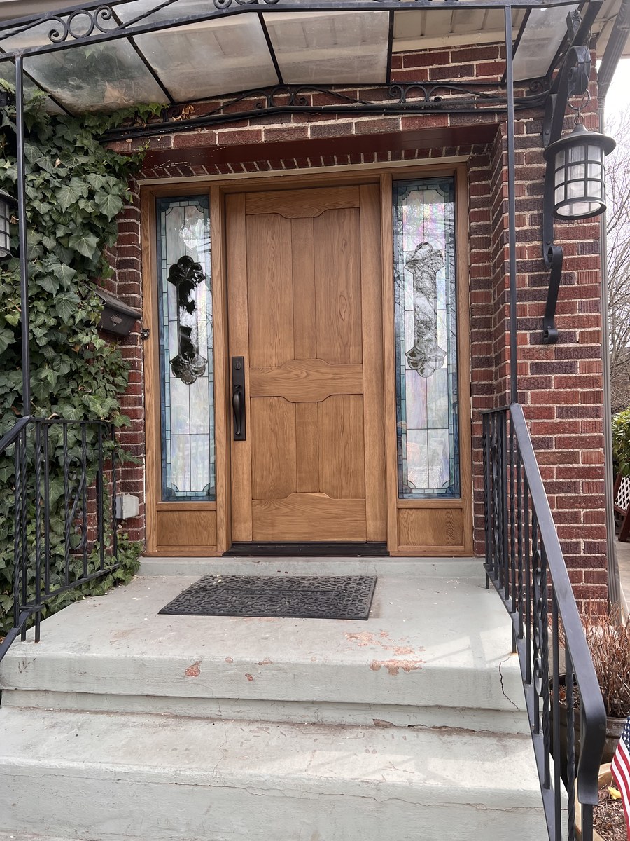 Custom wood entry door with decorative glass sidelights in a brick home